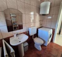 A bathroom with a mirror, sink, washing machine, and toilet in a 2-room apartment.