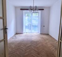 An empty room with a wooden floor, a large window, and a chandelier in a two-room apartment.