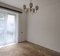 A room in a 2-room apartment with parquet floors and a large window with white curtains.