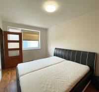 A bedroom with a double bed, a door, and a large window in a two-room apartment.