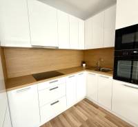 A kitchen in a 2-room apartment with white cabinets and a wooden countertop.
