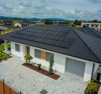 A family house in Piešťany with photovoltaic panels on the roof is surrounded by a green garden.