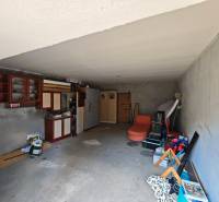 The interior of a garage in a family house with shelves, cabinets, and various stored equipment.