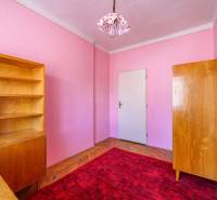 A room in a family house with wooden furniture, a red carpet, and pink walls.