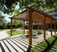 A wooden pergola with benches in a park in Košice, Juh district, surrounded by greenery.