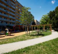 A playground with an apartment building in Košice - Juh district, surrounded by greenery and a walkway.