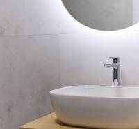 Bathroom with a sink on a wooden cabinet and an illuminated round mirror in a two-room apartment.