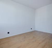 An empty room with white walls and wooden flooring in a two-room apartment.