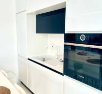 A kitchen in a 2-room apartment with a minimalist white unit and a built-in oven.
