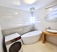 A bathroom in a 2-room apartment with a bathtub, sink, washing machine, and round mirror.