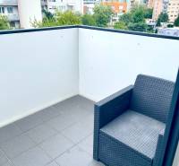 A balcony of a 2-room apartment with a rattan chair and a view of the surrounding apartment buildings.