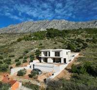 A villa in Duće surrounded by greenery and mountains with a blue sky in the background.