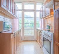 A kitchen with wooden furniture and appliances, light streaming through a large window.