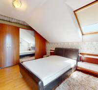 Attic bedroom in a family house with a double bed, mirrored wardrobe, and skylight.