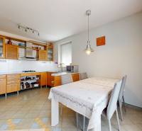 A kitchen in a family house with wooden cabinets, a dining table, and a tiled floor.