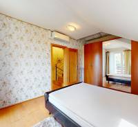 Bedroom in a family house with a bed, wardrobes, wallpaper, and a mirror.