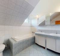 A family house bathroom with a bathtub and sinks, tiled with light tiles.
