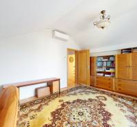 A room with a carpet, a bookshelf, and a writing desk in a family house.