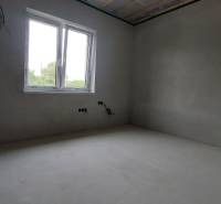An empty room in a family house with a plastic window and an unfinished ceiling.
