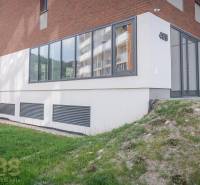 The facade of commercial spaces in the town of Svit with large windows and a green lawn.