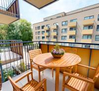 A balcony with wooden furniture in a 2-room apartment. View of the neighboring building and greenery.