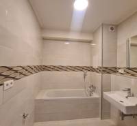 Bathroom in a studio apartment with a bathtub and a sink, ceramic tiles with a design strip.