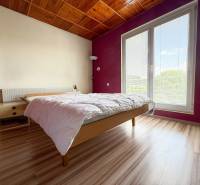 Bright bedroom in a family house with a wooden ceiling and a large window.