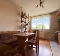 A family house with a kitchen containing wooden furniture, a dining table, and a shelf with decorations.