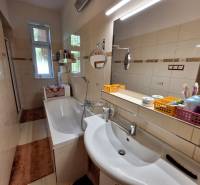 Bathroom with a bathtub and a mirror in a family house, equipped with shelves and a sink.
