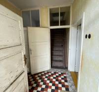 Entrance hallway in a family house with a checkered floor and wooden stairs.