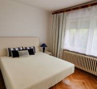 Bright bedroom in a family house with a bed, lamp, and wooden floor.