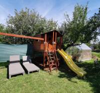 The garden of a family house in Topoľčianky with a children's playhouse, slide, and loungers.