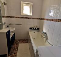 A bathroom in a family house with a built-in bathtub and sink, tiled with light tiles.