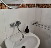 A sink in a family house with a round mirror and tiles with a brown pattern.
