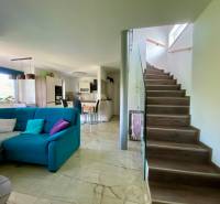 Living room with kitchen in a family house, staircase, comfortable couch, and dining table.
