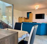 Living room in a family house with a blue sofa, dining table, and a TV on the wall.