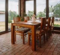 Dining table with six chairs, brick floor, large windows in a family house.
