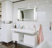 A bathroom in a family house with a washing machine, water heating, a sink, and a lighted mirror.