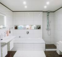 A bathroom in a family house with white tiles, a bathtub, and a shower.