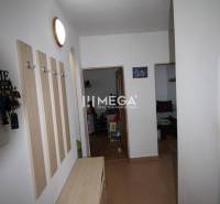 A hallway in a 2-room apartment with furniture, coat racks, and open doors to the rooms.