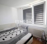 Bedroom in a 2-room apartment with a bed, a baby crib, and a large window.