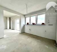 An empty room in a family house with three large windows and a concrete floor.