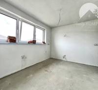 An empty room in a family house with large windows and an unfinished floor.