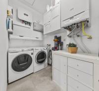 Laundry room in a family house with a washing machine, dryer, storage cabinets, and a boiler.