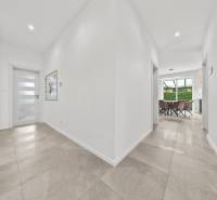 A hallway of a family house with tiles and an entrance to the dining room with a glass wall.