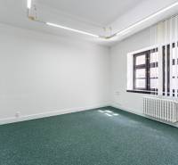 An office with white walls, green carpet, and windows with vertical blinds.