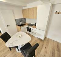 A kitchen in a studio apartment with a wooden floor, a dining table, and white cabinets.
