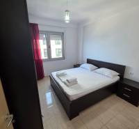 A bedroom in a holiday apartment with a double bed, nightstands, and a window with red curtains.