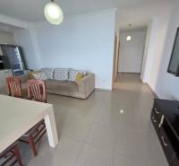 A bright living room with a kitchenette, a sofa, and a dining table in a holiday apartment.