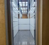 Illuminated interior of an elevator in a 3-room apartment with glass walls and tiled floor.